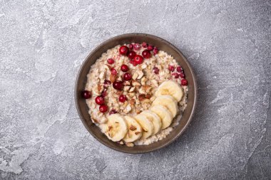 Taze yulaf ezmesi, fındık ve muz dilimleri ile sağlıklı kahvaltı için gri beton arka planda.