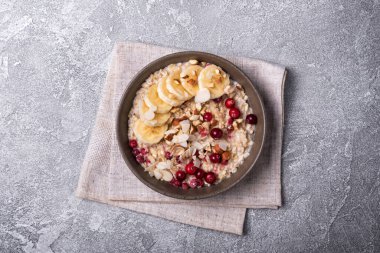 Taze yulaf ezmesi, fındık ve muz dilimleri ile sağlıklı kahvaltı için gri beton arka planda.