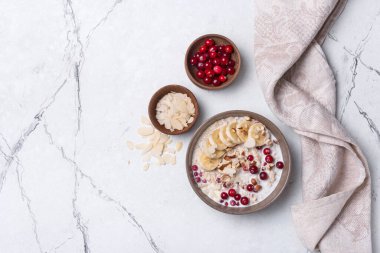 Beyaz mermer arka planda sağlıklı kahvaltı için yulaf ezmesi, fındık, badem ve muz dilimleri.