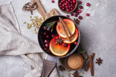 Elmalar, portakallar, kızılcık, tarçın, biberiye ve gri beton arka plandaki diğer malzemelerle sonbahar ya da Noel içeceği