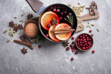 Elmalar, portakallar, kızılcık, tarçın, biberiye ve gri beton arka plandaki diğer malzemelerle sonbahar ya da Noel içeceği