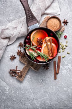 Elmalar, portakallar, kızılcık, tarçın, biberiye ve gri beton arka plandaki diğer malzemelerle sonbahar ya da Noel içeceği
