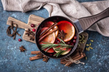 Elmalar, portakallar, kızılcık, tarçın, biberiye ve mavi beton arka plandaki diğer malzemelerle sonbahar ya da Noel içeceği