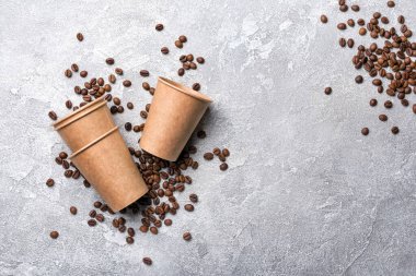 Kavrulmuş kahve çekirdekleri ve gri beton arka planda sabah espresso için tek kullanımlık kağıt bardak.