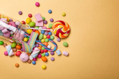 Altın arka planda eğlence partisi için çok renkli tatlı ve parlak dragee, şekerleme ve lokum dolu cam kavanoz.