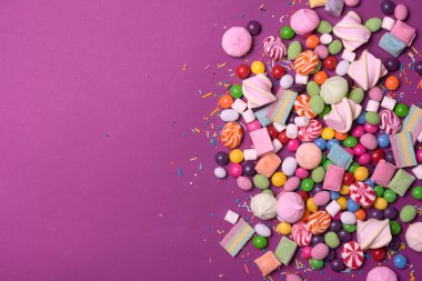 Çok renkli tatlı ve parlak dragee, şekerler, lolipoplar, mor arka plandaki eğlence partisi için şekerlemeler