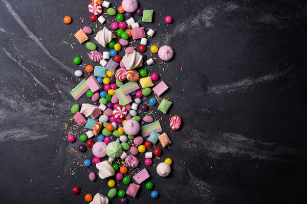 Multicolored sweet and bright dragee, candies, lollipops, marshmallows for fun party on black marble background