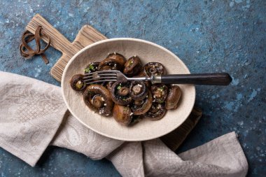 Mavi beton arka planda baharatlı ızgara şampiyon mantarlarının en üst görüntüsü.