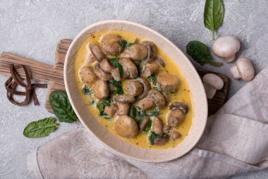 Ispanak yaprakları ve krema soslu gri beton arka planda şampiyon mantarlarının en üst görüntüsü.