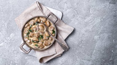 Ispanak yaprakları ve krema sosuyla kızartma tavasında gri beton arka planda şampiyon mantarlarının üst görüntüsü