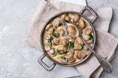 Ispanak yaprakları ve krema sosuyla kızartma tavasında gri beton arka planda şampiyon mantarlarının üst görüntüsü