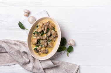 Beyaz ahşap arka planda ıspanak yaprakları ve krema soslu şampiyon mantarları.