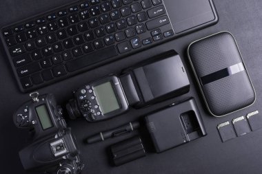 Fotoğrafçı çalışma alanının en üst görüntüsü dijital kamera, flash, hafıza kartı, klavye, taşınabilir sabit disk ile siyah arka groun