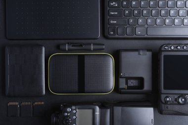 Fotoğrafçı çalışma alanının en üst görüntüsü dijital kamera, flash, hafıza kartı, klavye, taşınabilir sabit disk ile siyah arka groun