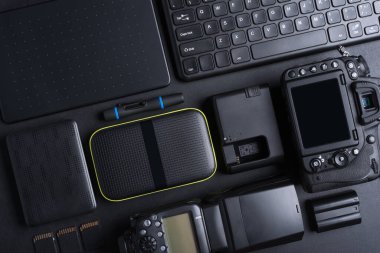 Fotoğrafçı çalışma alanının en üst görüntüsü dijital kamera, flash, hafıza kartı, klavye, taşınabilir sabit disk ile siyah arka groun