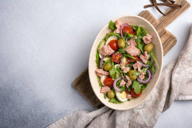 Ton balıklı sağlıklı ve lezzetli salata, taze roka, vişneli domates, bıldırcın yumurtası, soğan ve yeşil zeytinli gri beton zemin