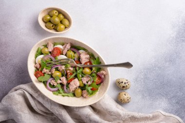 Ton balıklı sağlıklı ve lezzetli salata, taze roka, vişneli domates, bıldırcın yumurtası, soğan ve yeşil zeytinli gri beton zemin