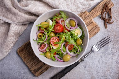 Sağlıklı ve lezzetli vejetaryen yemeklerinin en üst görüntüsü. Taze roka yapraklı salata, kiraz domatesleri, bıldırcın yumurtası, soğan ve gri betonda yeşil zeytin.