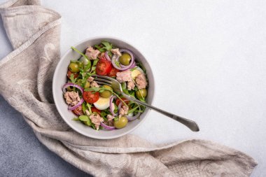 Ton balıklı sağlıklı ve lezzetli salata, taze roka, vişneli domates, bıldırcın yumurtası, soğan ve yeşil zeytinli gri beton zemin