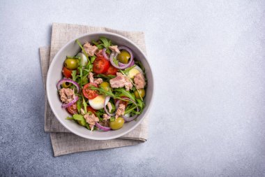 Ton balıklı sağlıklı ve lezzetli salata, taze roka, vişneli domates, bıldırcın yumurtası, soğan ve yeşil zeytinli gri beton zemin