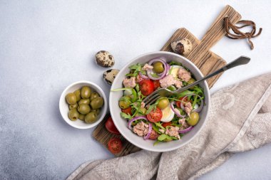 Ton balıklı sağlıklı ve lezzetli salata, taze roka, vişneli domates, bıldırcın yumurtası, soğan ve yeşil zeytinli gri beton zemin