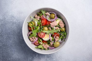 Ton balıklı sağlıklı ve lezzetli salata, taze roka, vişneli domates, bıldırcın yumurtası, soğan ve yeşil zeytinli gri beton zemin