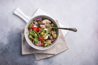 Ton balıklı sağlıklı ve lezzetli salata, taze roka, vişneli domates, bıldırcın yumurtası, soğan ve yeşil zeytinli gri beton zemin