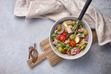 Ton balıklı sağlıklı ve lezzetli salata, taze roka, vişneli domates, bıldırcın yumurtası, soğan ve yeşil zeytinli gri beton zemin
