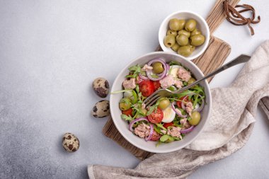 Ton balıklı sağlıklı ve lezzetli salata, taze roka, vişneli domates, bıldırcın yumurtası, soğan ve yeşil zeytinli gri beton zemin