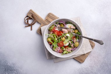 Ton balıklı sağlıklı ve lezzetli salata, taze roka, vişneli domates, bıldırcın yumurtası, soğan ve yeşil zeytinli gri beton zemin