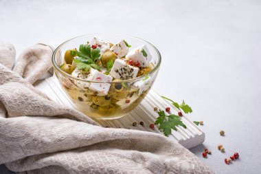 Feta peynirli, biberli, yeşil zeytinli cam kasede taze maydanoz ve gri beton arka planda yağlı.