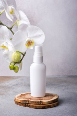 Cilt kozmetik ürününün bir kopyası. Beyaz eko losyon şişesi ahşap kaidede ve modern gri arka planda güzel orkide çiçekleri var.