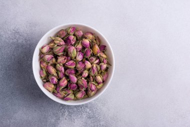 Beyaz kasenin en üst görüntüsü kuru gül tomurcukları ile kokulu çay için gri beton arka planda