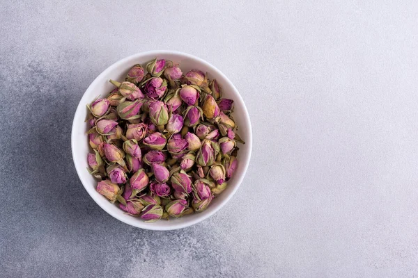 Beyaz kasenin en üst görüntüsü kuru gül tomurcukları ile kokulu çay için gri beton arka planda