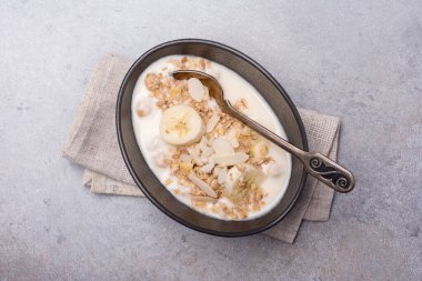 Sağlıklı kahvaltı için yoğurtlu granola, taze muz ve badem fıstığı gri beton arka planda.