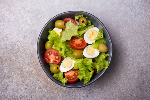 Sağlıklı ve lezzetli salata, taze marul, vişneli domates, bıldırcın yumurtası ve gri beton arka planda yeşil zeytinler.