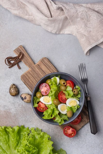 Sağlıklı ve lezzetli salata, taze marul, vişneli domates, bıldırcın yumurtası ve gri beton arka planda yeşil zeytinler.
