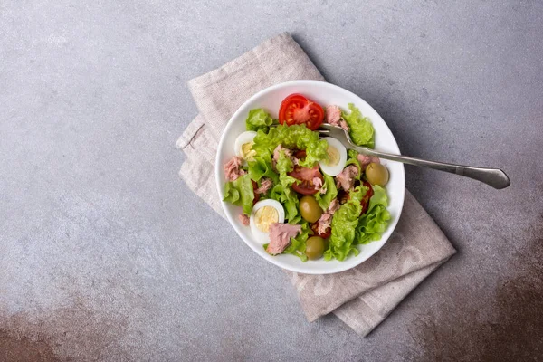 Ton balıklı sağlıklı ve lezzetli salata, taze marul, vişneli domates, bıldırcın yumurtası ve yeşil zeytinli gri betli arka plan.