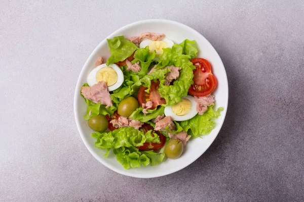 Ton balıklı sağlıklı ve lezzetli salata, taze marul, vişneli domates, bıldırcın yumurtası ve yeşil zeytinli gri betli arka plan.