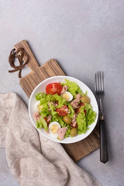 Ton balıklı sağlıklı ve lezzetli salata, taze marul, vişneli domates, bıldırcın yumurtası ve yeşil zeytinli gri betli arka plan.