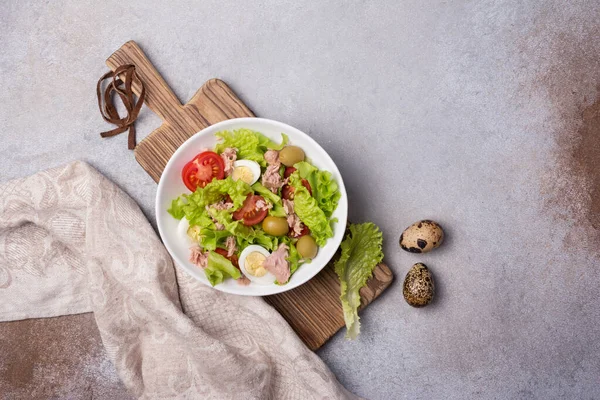 Ton balıklı sağlıklı ve lezzetli salata, taze marul, vişneli domates, bıldırcın yumurtası ve yeşil zeytinli gri betli arka plan.