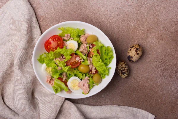 Ton balıklı sağlıklı ve lezzetli salata, taze marul, kiraz domatesleri, bıldırcın yumurtası ve kahverengi beton arka planda yeşil zeytinler.