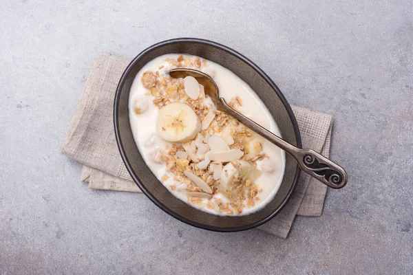 Sağlıklı kahvaltı için yoğurtlu granola, taze muz ve badem fıstığı gri beton arka planda.