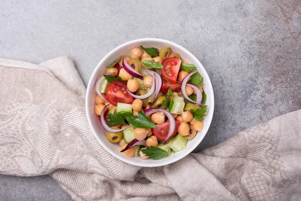 Healthy and tasty vegan food. Top view of chickpea salad with lettuce, cherry tomatoes, onion, cucumber and green olives on grey concrete background