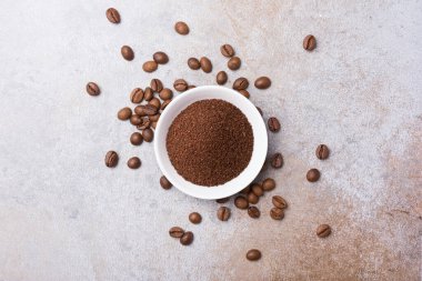 Gri beton arka planda beyaz kasede öğütülmüş kahve ile kavrulmuş fasulye manzarası
