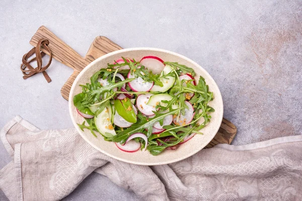 Sağlıklı ve lezzetli vejetaryen yemekleri. Turp, salatalık, soğan, taze yeşil yapraklar ve hardal soslu gri çimento arkaplanlı hafif salata.