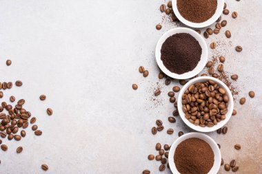 Fotokopi alanı olan gri beton arka planda, beyaz kâselerde öğütülmüş kahve ile kavrulmuş fasulye manzarası.
