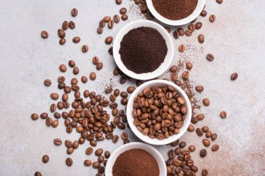 Gri arka planda beyaz kâselerde öğütülmüş kahve ile kavrulmuş fasulye manzarası