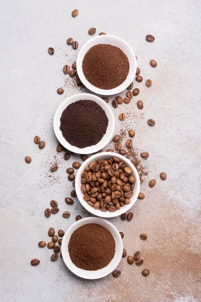 Gri arka planda beyaz kâselerde öğütülmüş kahve ile kavrulmuş fasulye manzarası