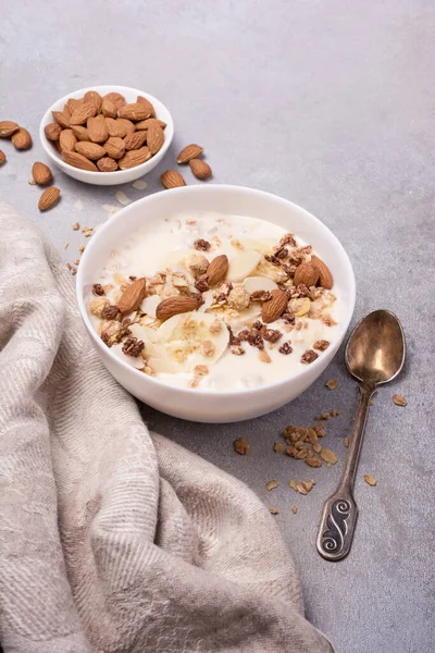Sağlıklı kahvaltı için yoğurtlu granola, taze muz ve badem fıstığı gri beton arka planda.